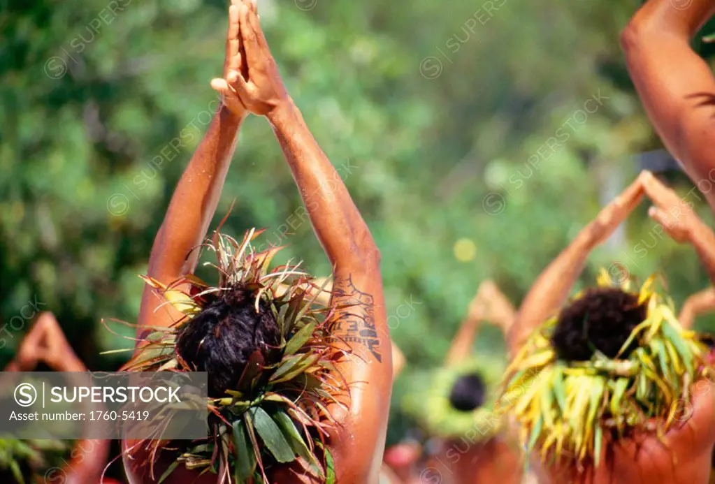 French Polynesia, Tahiti, View from behind Tahitian men dancing outdoors, arms raised, wearing haku on head