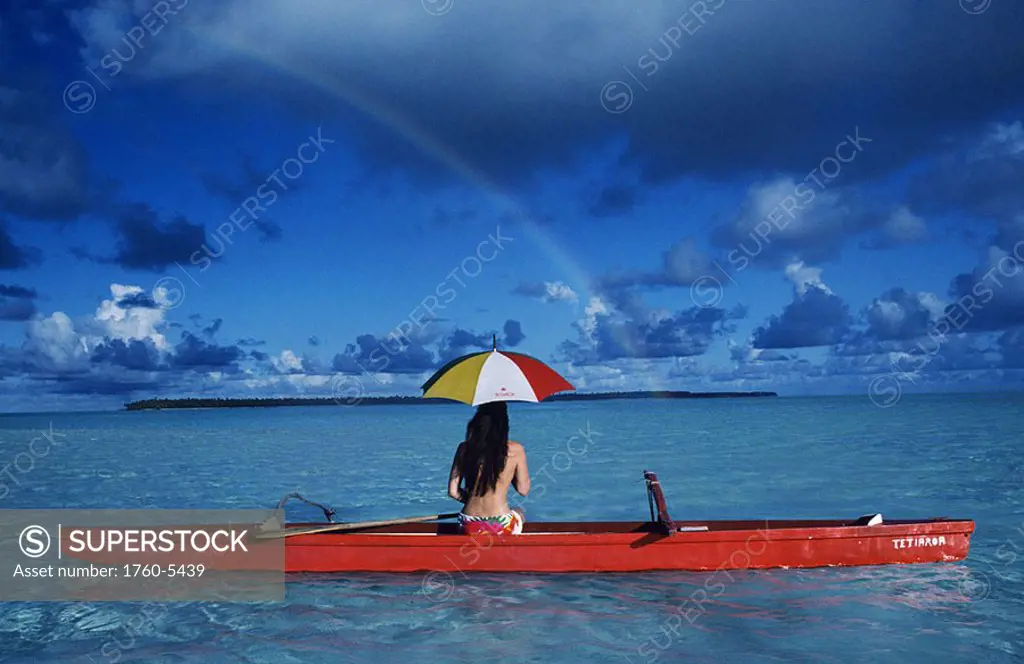 French Polynesia, Tetiaroa, Woman with umbrella in outrigger canoe floating on clear turquoise ocean, View from behind