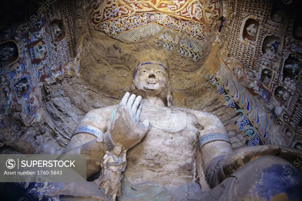 China, Datong, Yungang Caves, detail of large statue seen from below, surrounded by colorful paintings and carvings