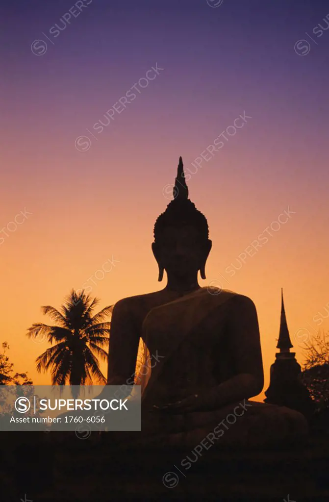 Thailand, Sukhothai, Wat Mahathat at sunset, silhouetted Buddha statue, purple and orange sky.