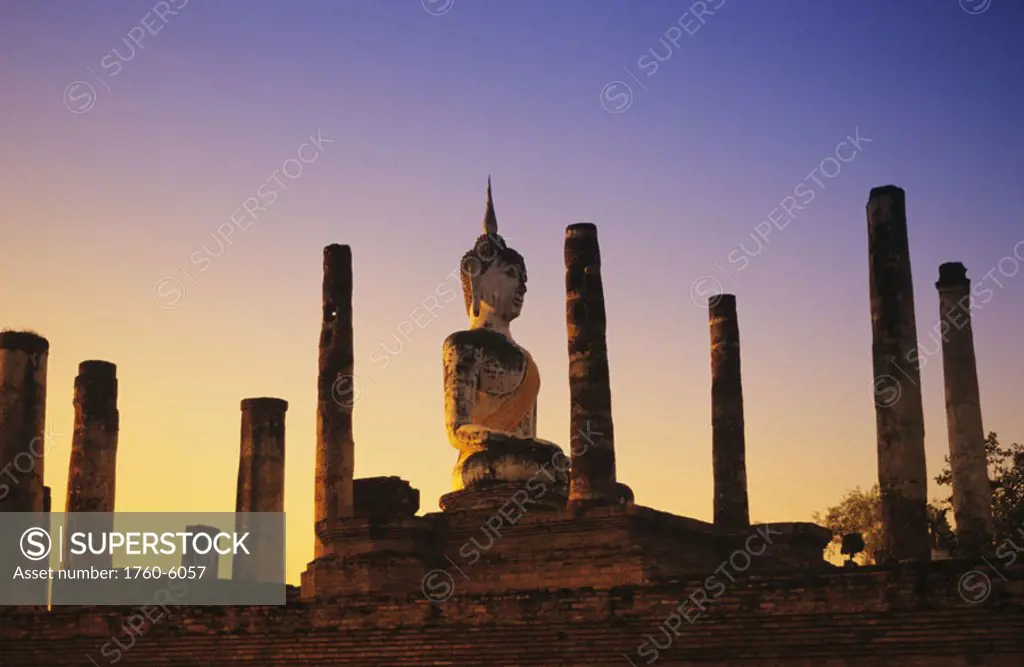 Thailand, Sukhothai, Wat Mahathat, Buddha statue with many pillars at sunset, blue and orange sky.
