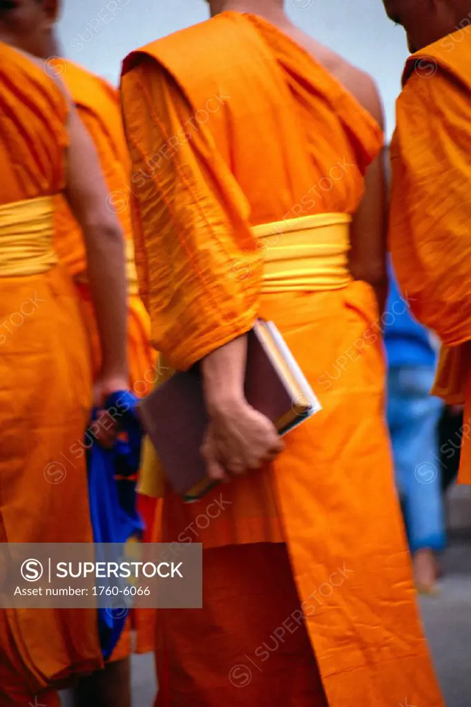Thailand, back view of Buddist monks walking with book, orange robes C1901