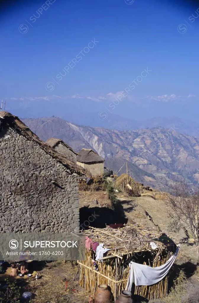 Nepal, high altitude village near Nagarkot, woman sitting outside brick home with children, mountains in distance.