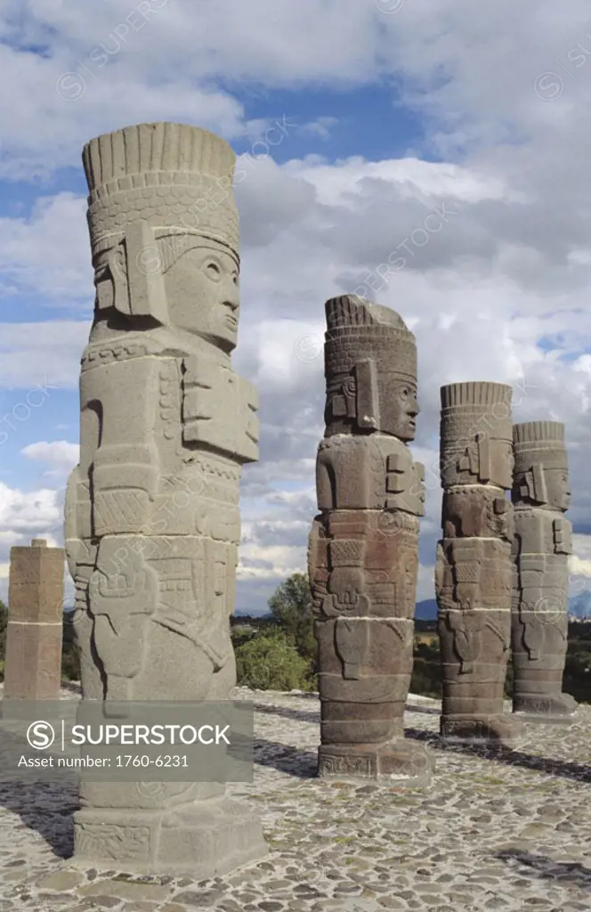 Mexico, Tula, Toltec Ruins, stone sculptures lined up in row,  clouds and blue sky above, angled view.
