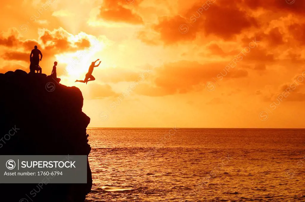 Hawaii, Oahu, North Shore, Waimea Bay, Silhouette of boys jumping from rock at sunset 