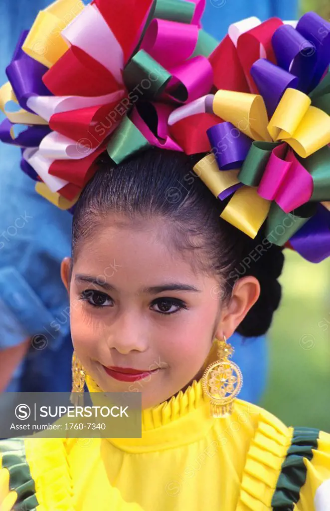 Mexico, portrait of girl in traditional outfit, brightly colored bows and gold earrings 