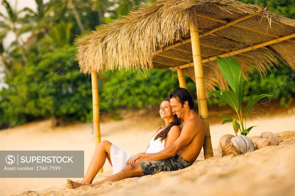 Man and Woman relaxing under thatched hut on beach