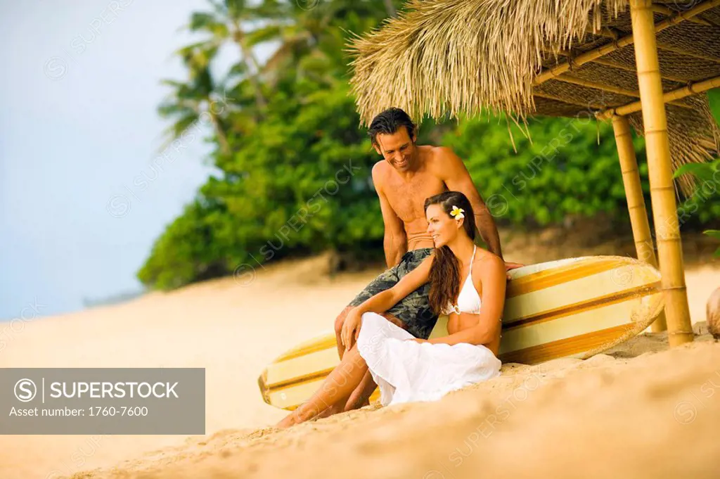 Man and woman relaxing under thatched hut on beach