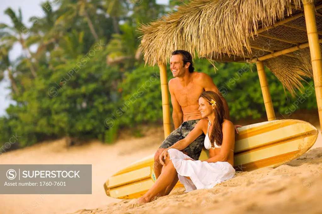 Man and Woman relaxing under thatched hut on beach