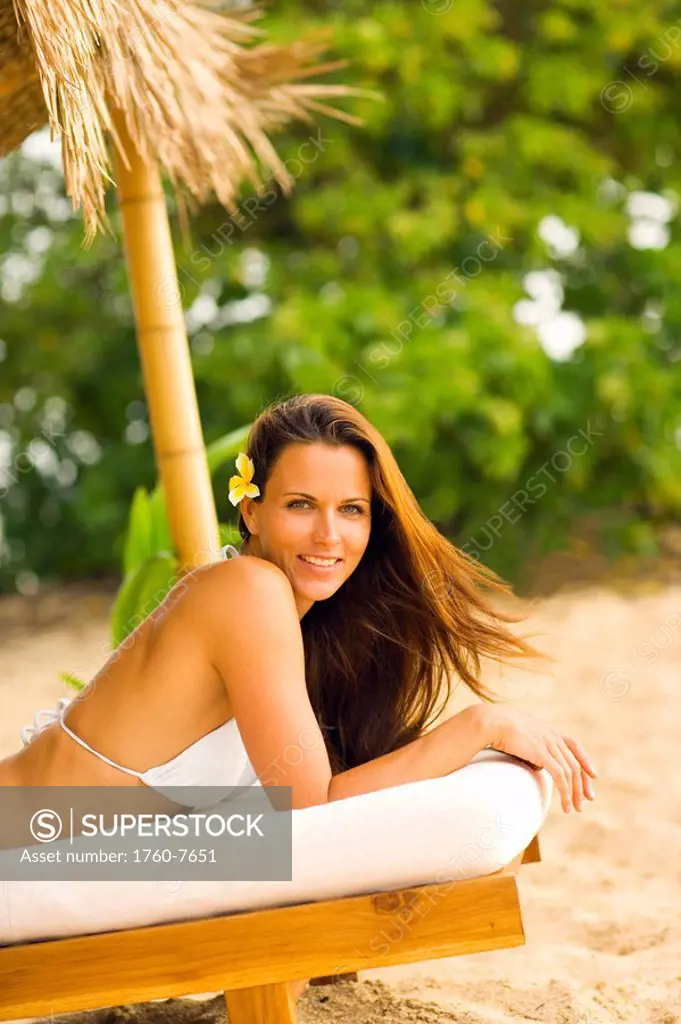 Woman on wooden lounge chair under thatched hut