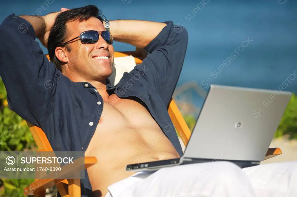 Hawaii, Handsome man sitting on beach with laptop computer.