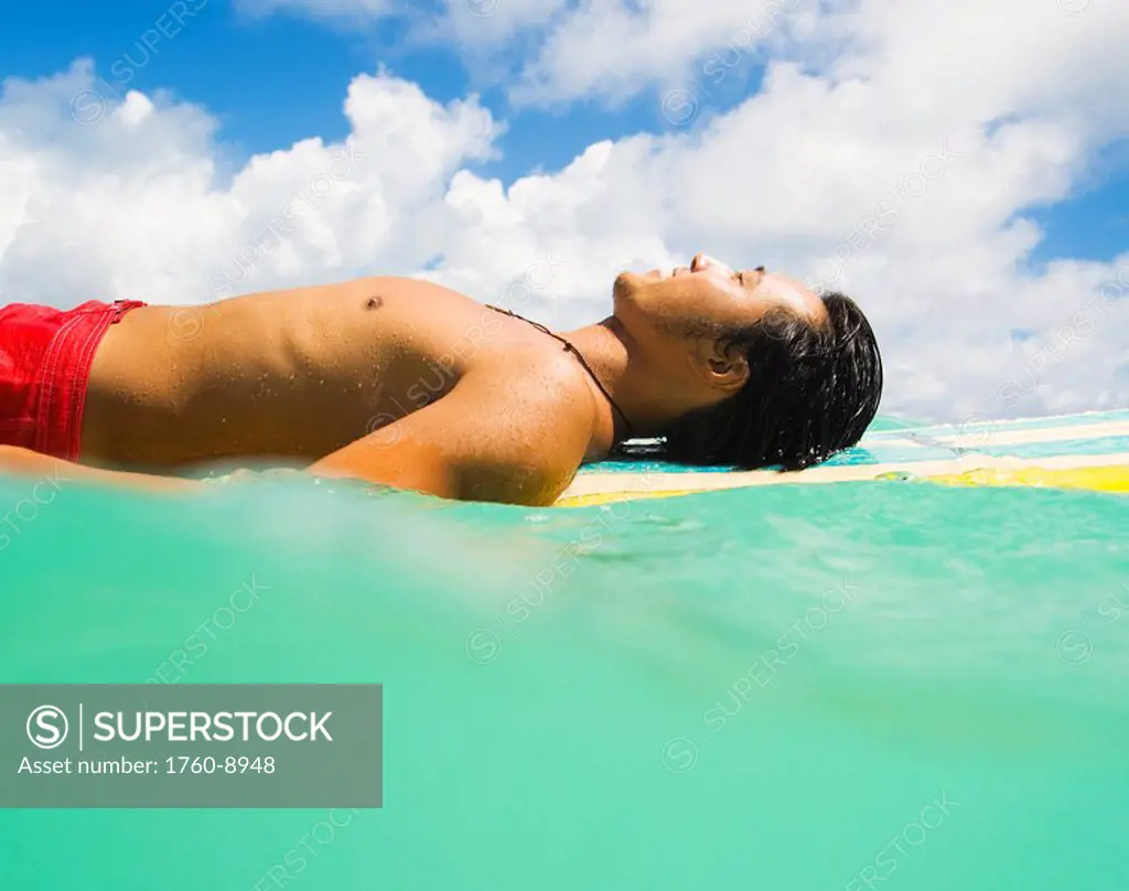 Hawaii, Oahu, Lanikai, Young Japanese man lying on surfboard in the ocean.