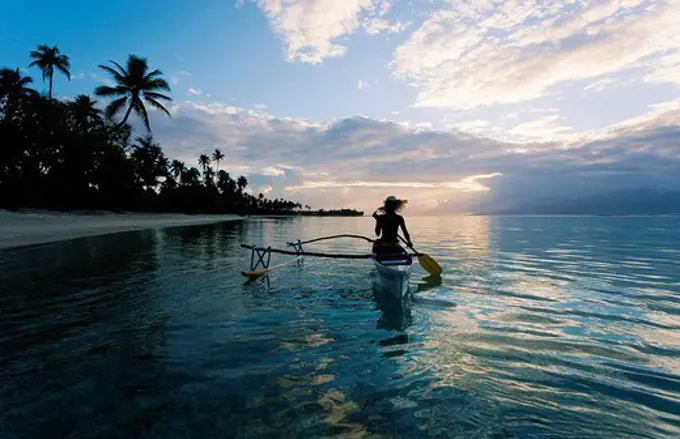 French Polynesia, Moorea, Woman paddling in outrigger canoe along shoreline.