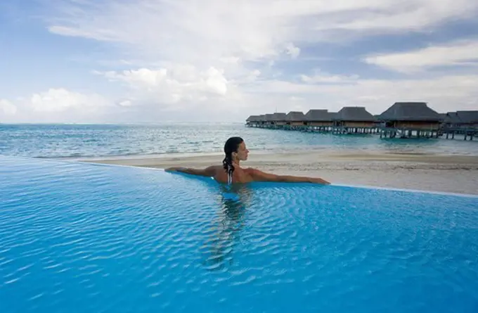 French Polynesia, Moorea, Woman relaxing in resort pool, Luxury resort bungalows in background.