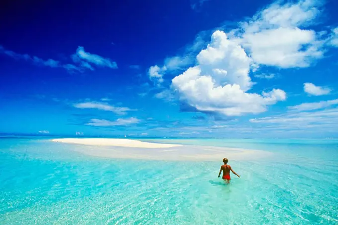 French Polynesia, Tahiti, Bora Bora, calm turquoise ocean surrounds sand islet, woman wading, view from behind