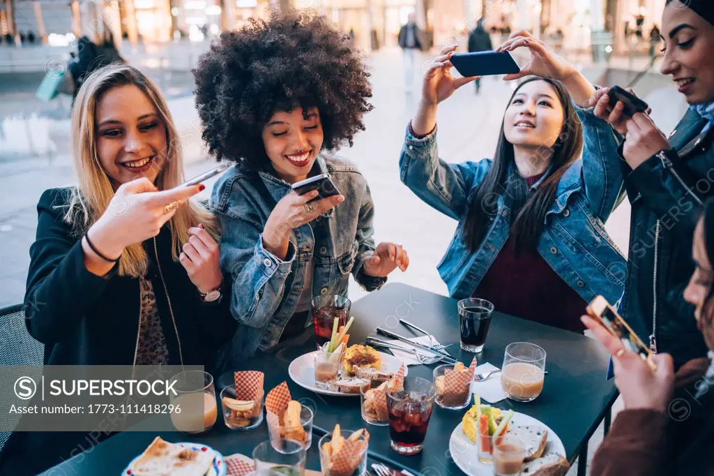 Friends taking photos of their food and drinks at outdoor cafe, Milan, Italy