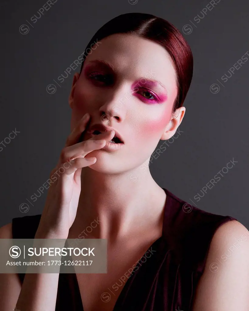 Portrait of young woman with heavy eye make-up, hand touching face