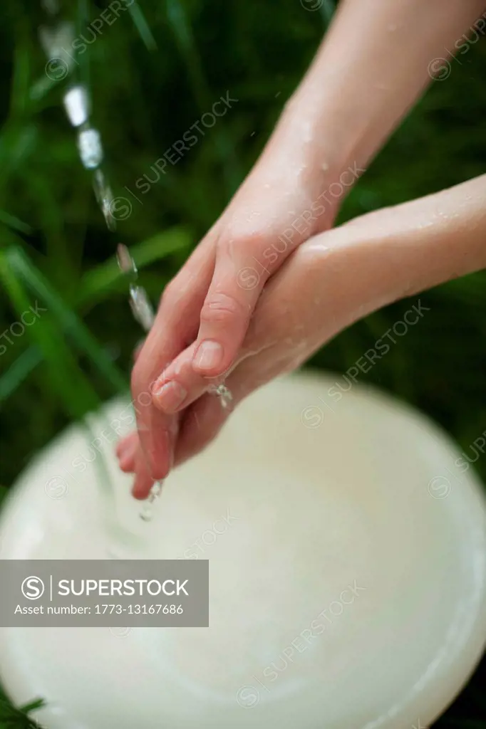 Young woman washing hands under flower water, close-up