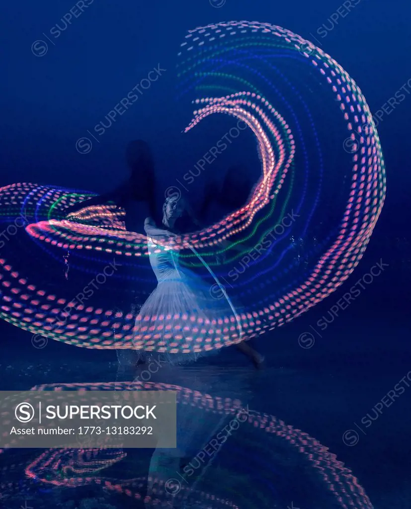 Woman dancing with illuminated multi-coloured hoop at dusk