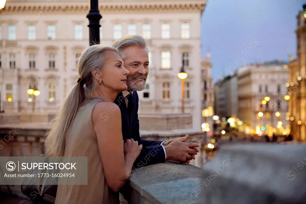 A couple leaning against a balustrade overlooking Vienna during the evening.