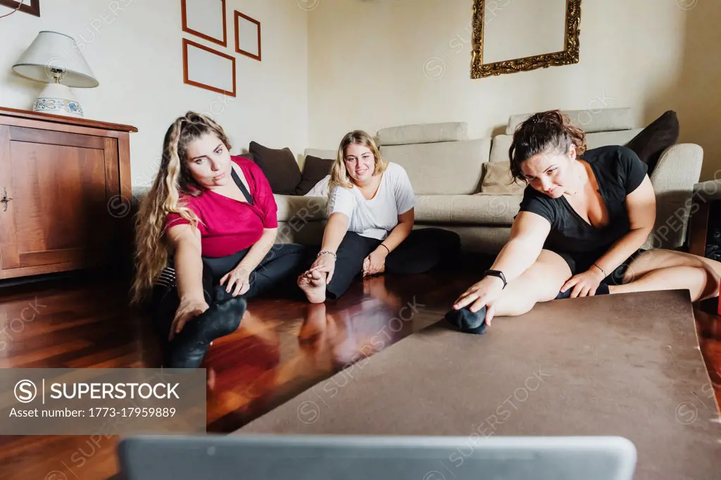 Female friends stretching, taking online exercise class together