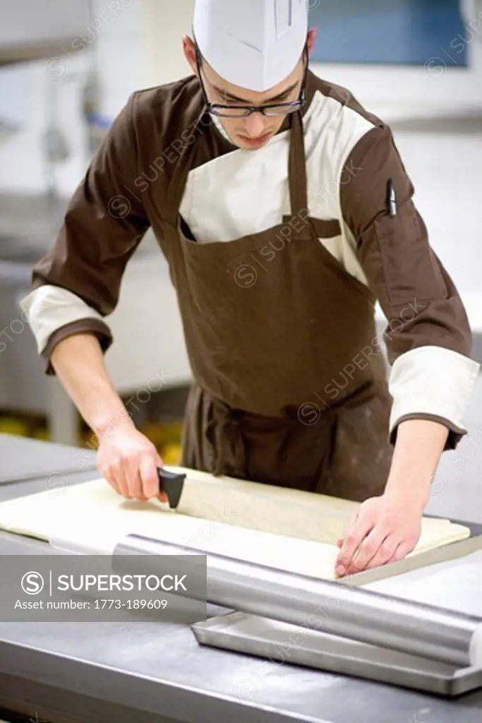 Baker slicing dough in kitchen