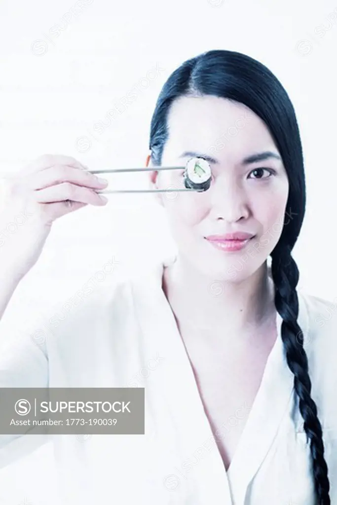 Woman holding piece of sushi over eye