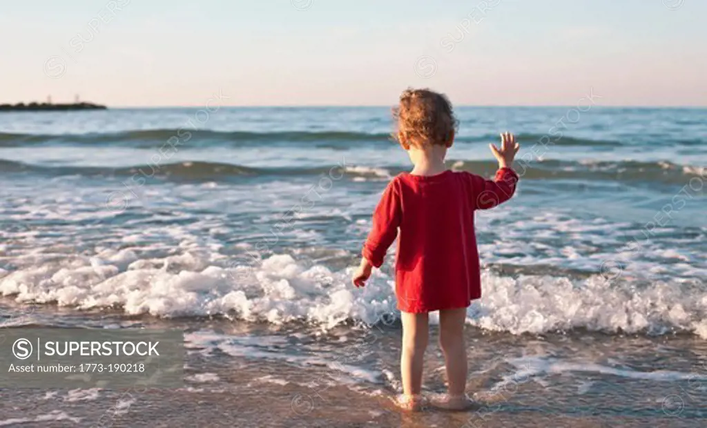 Toddler girl standing in waves on beach