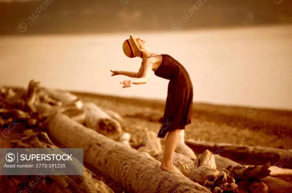 Woman standing on driftwood and stretching back