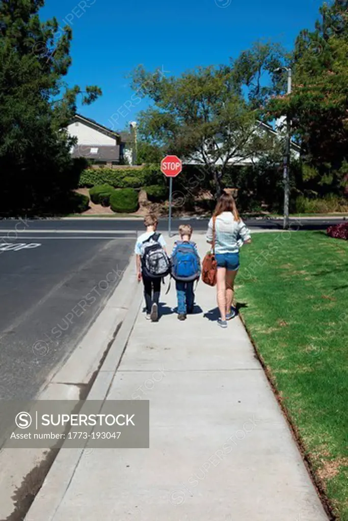 Teenage girl walking brothers to school along sidewalk