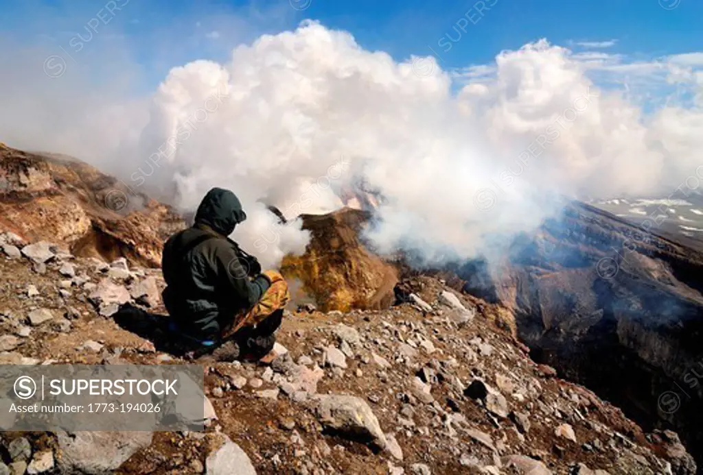 Man on edge of Gorely Volcano crater, looking at gas and steam plume, Kamchatka Peninsula, Russia
