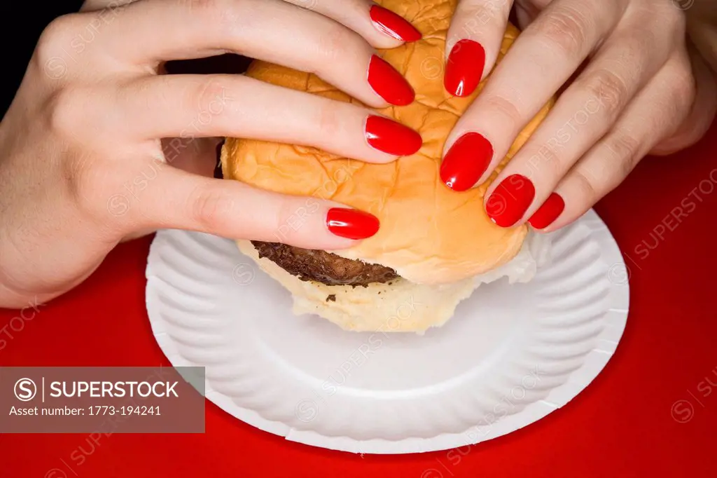 Woman with red fingernails holding burger