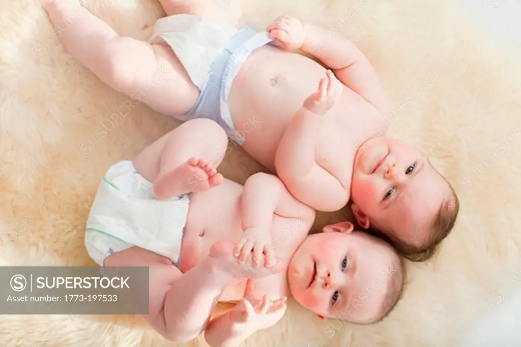 Twin baby girls lying on a sheepskin rug