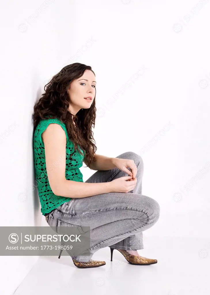 Woman crouching against white wall, portrait