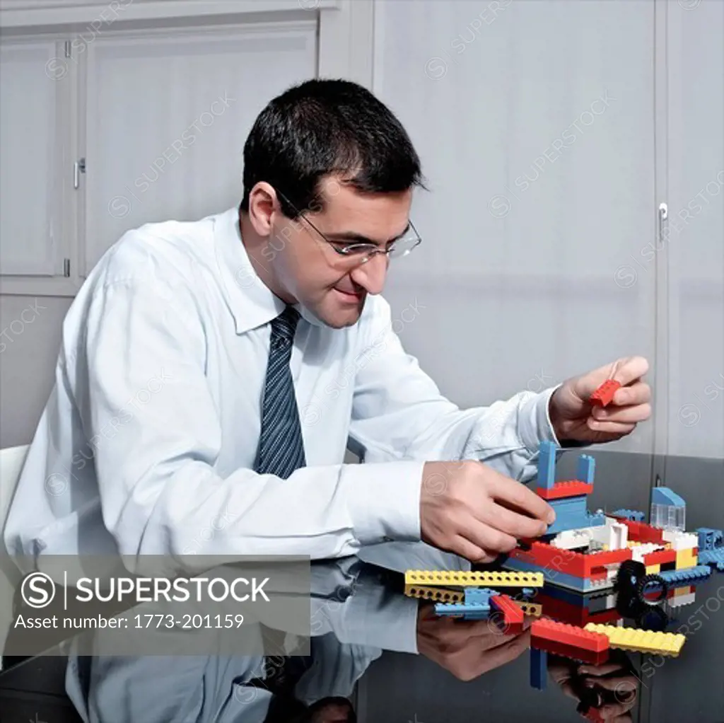 Mature businessman playing with plastic blocks at desk