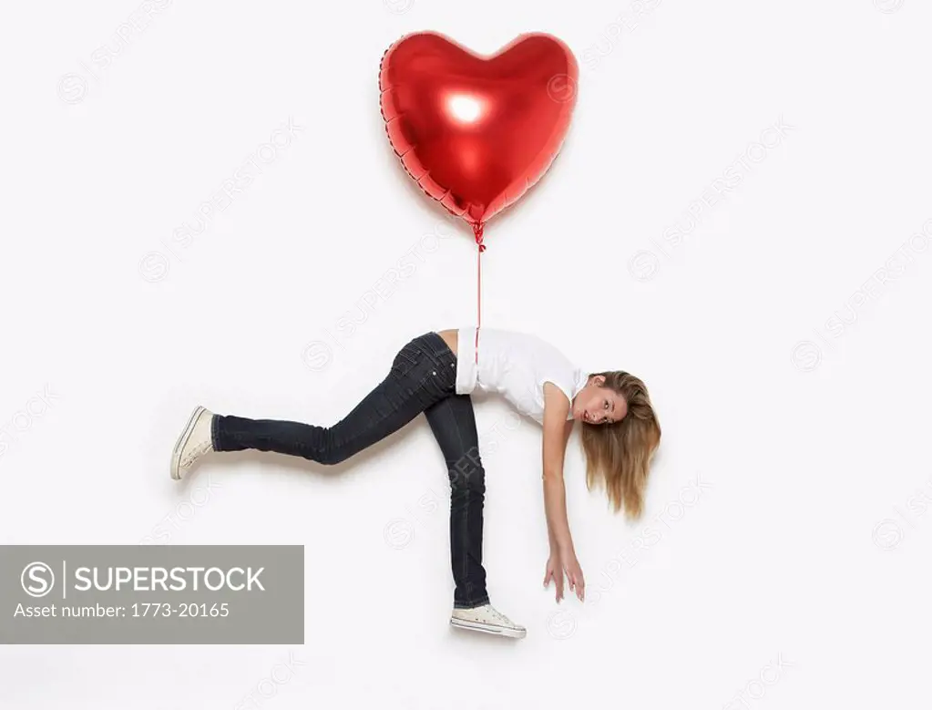 young woman being lifted away by heart shaped helium balloon
