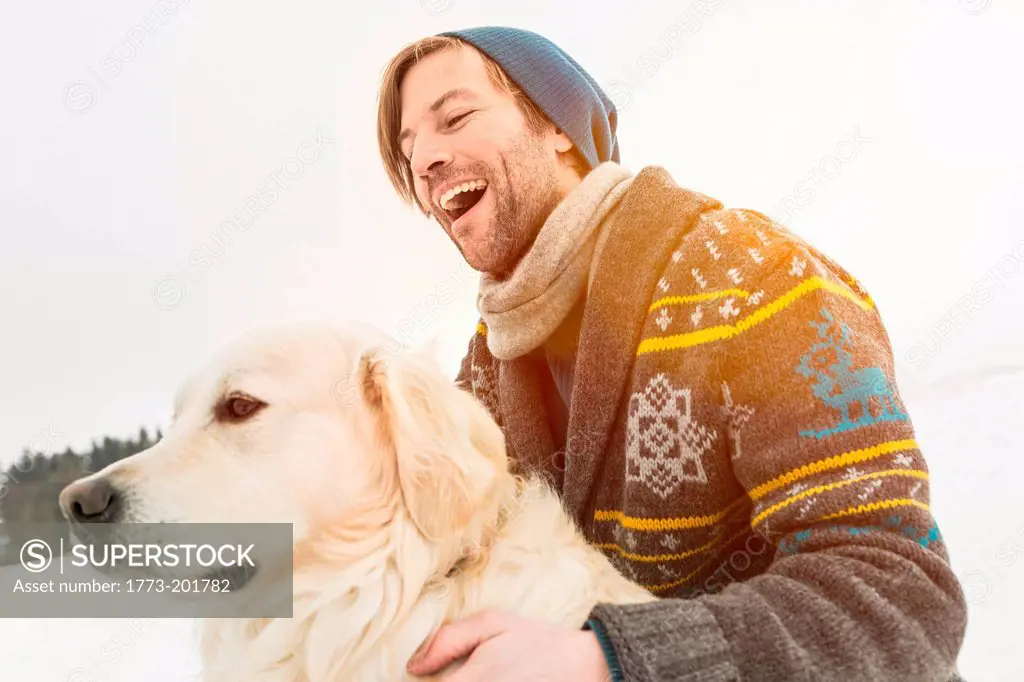 Man wearing knitted cardigan with dog in snow