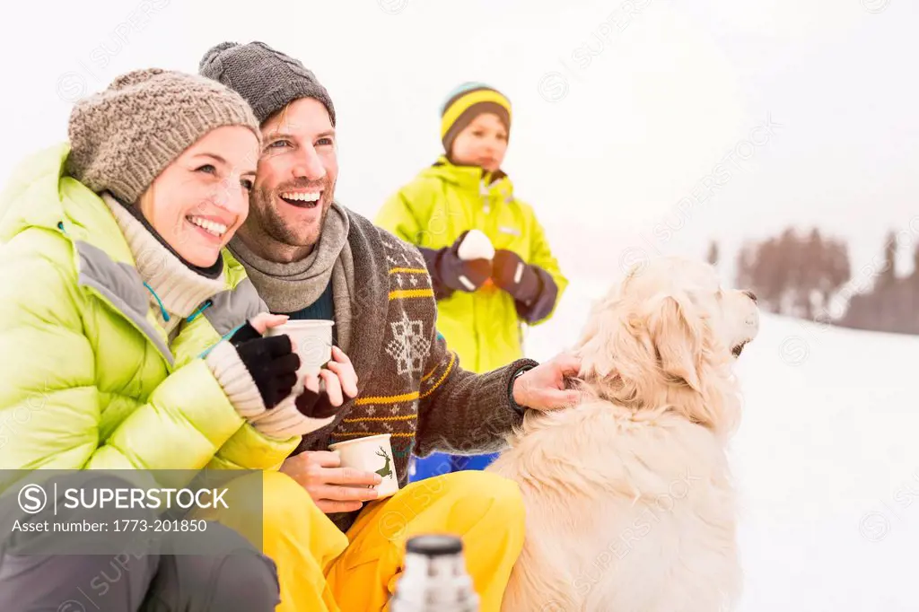 Man and woman with hot drinks and dog, son in background