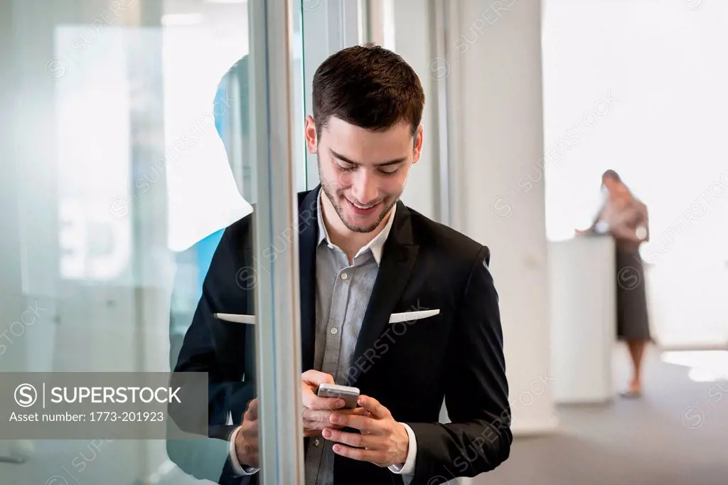 Businessman using cell phone, woman in background