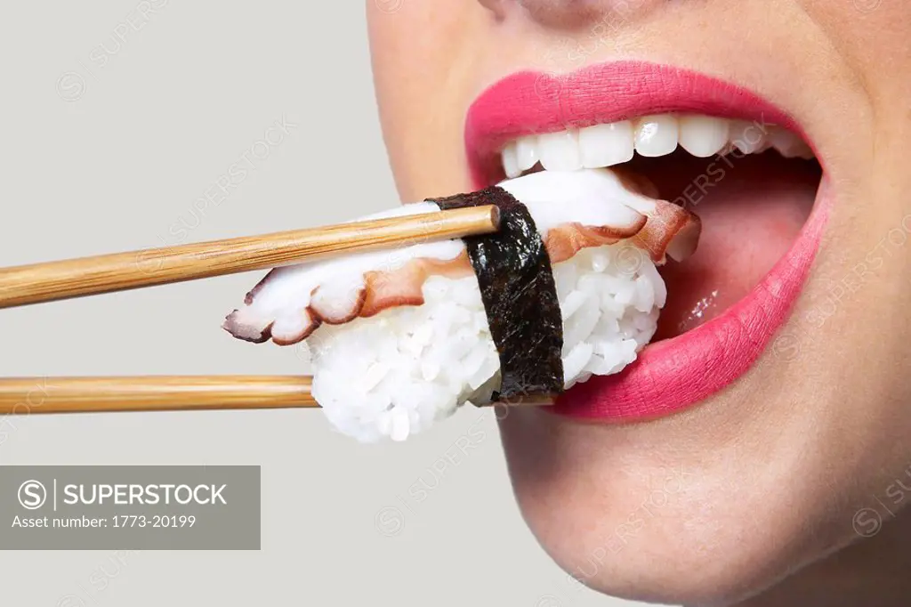 Close up of young woman using chop sticks to put sushi in her mouth