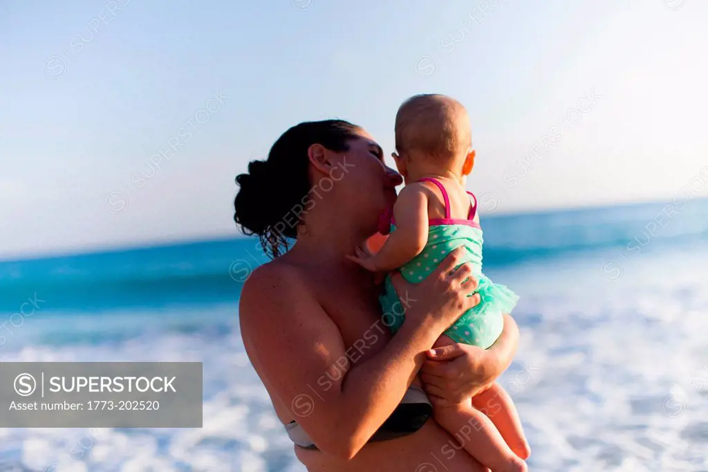 Mother holding baby daughter by sea, St Maarten, Netherlands