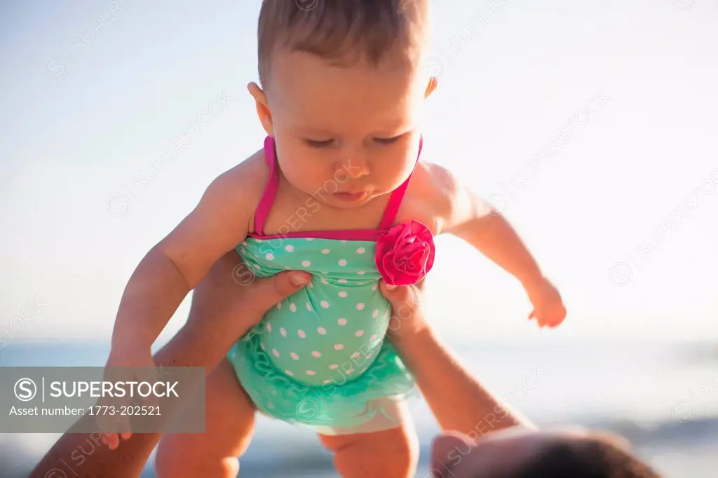 Woman lifting baby girl wearing swimsuit