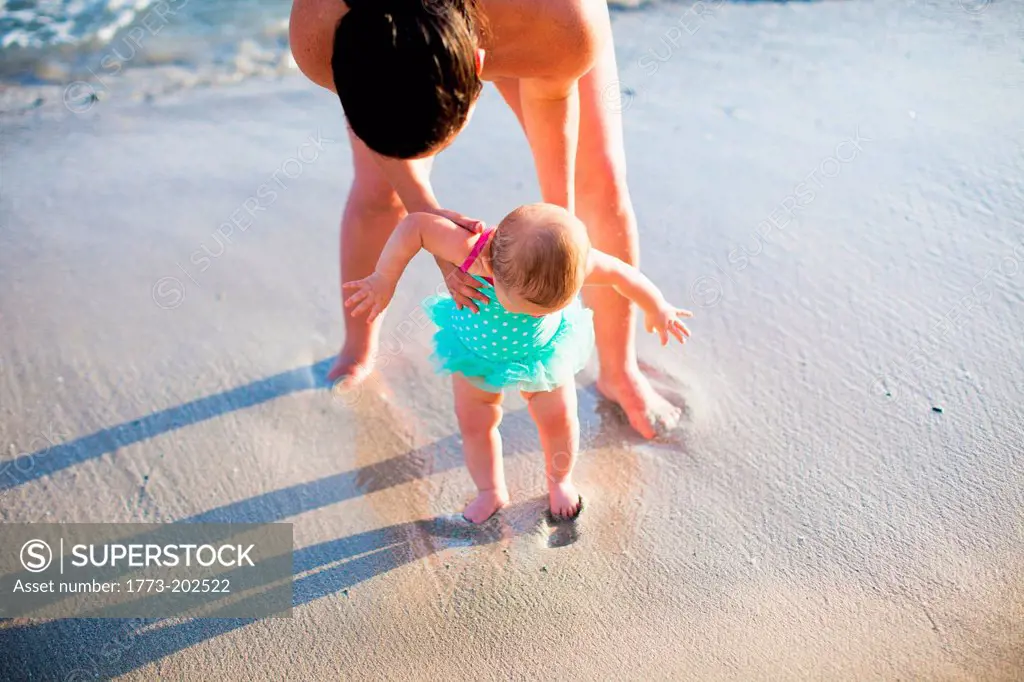 Mother helping baby daughter learn to walk on beach, St Maarten, Netherlands