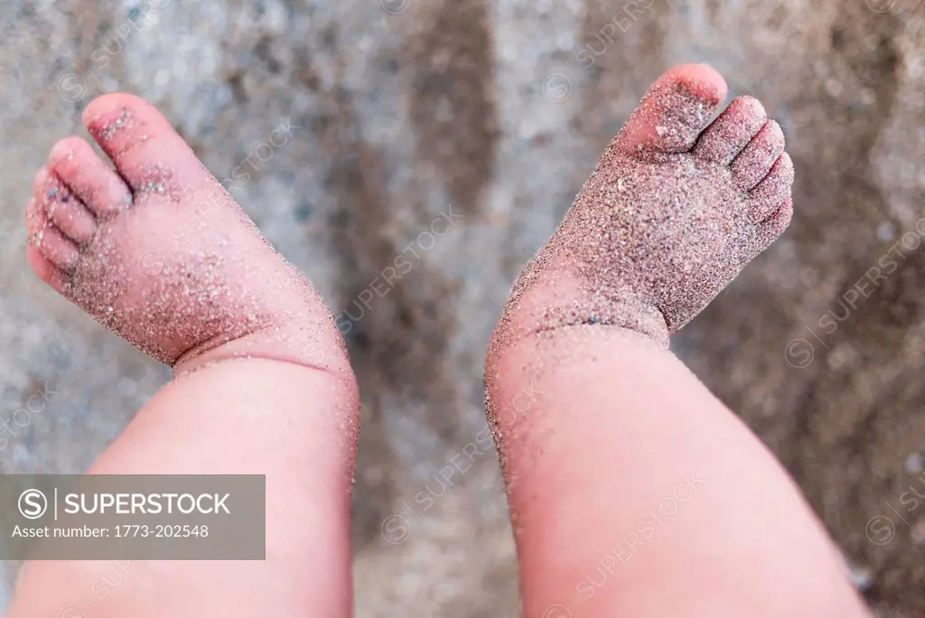 Baby girls bare feet covered in sand