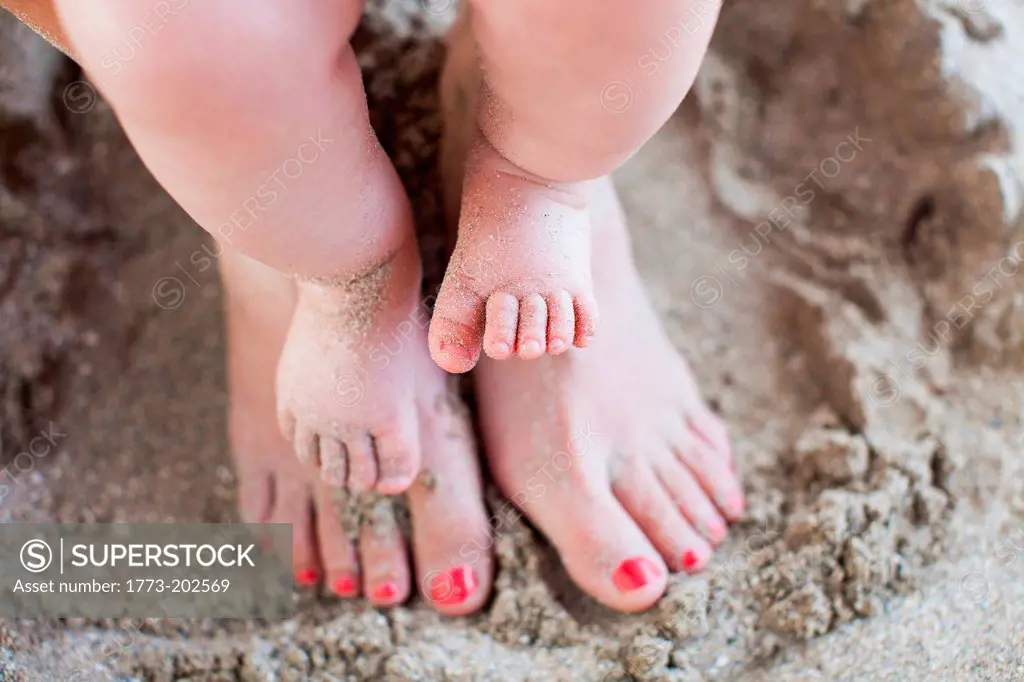 Mother with baby daughter's bare feet in sand
