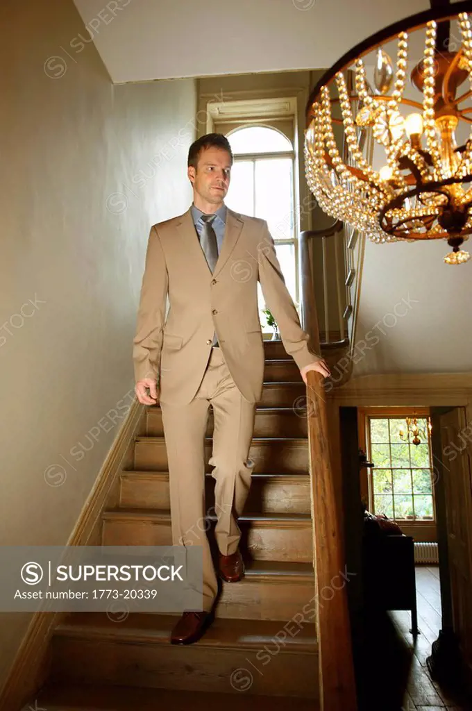 Man in beige suit walking down the stairs in elegant old house. He is looking to his side down the stairs.