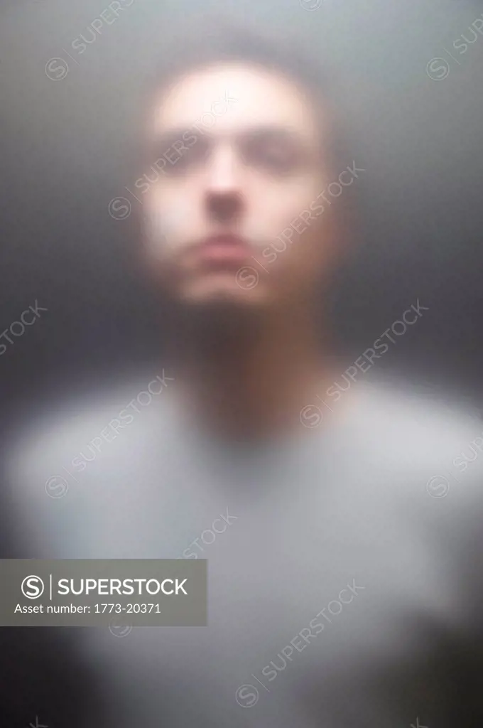 Blurred portrait of young man seen through frosted glass screen.