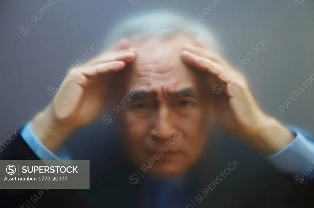 Blurred portrait of senior businessman peering through frosted screen with worried expression.