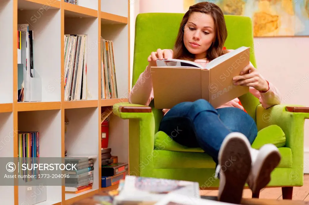 Young woman sitting in green armchair reading book