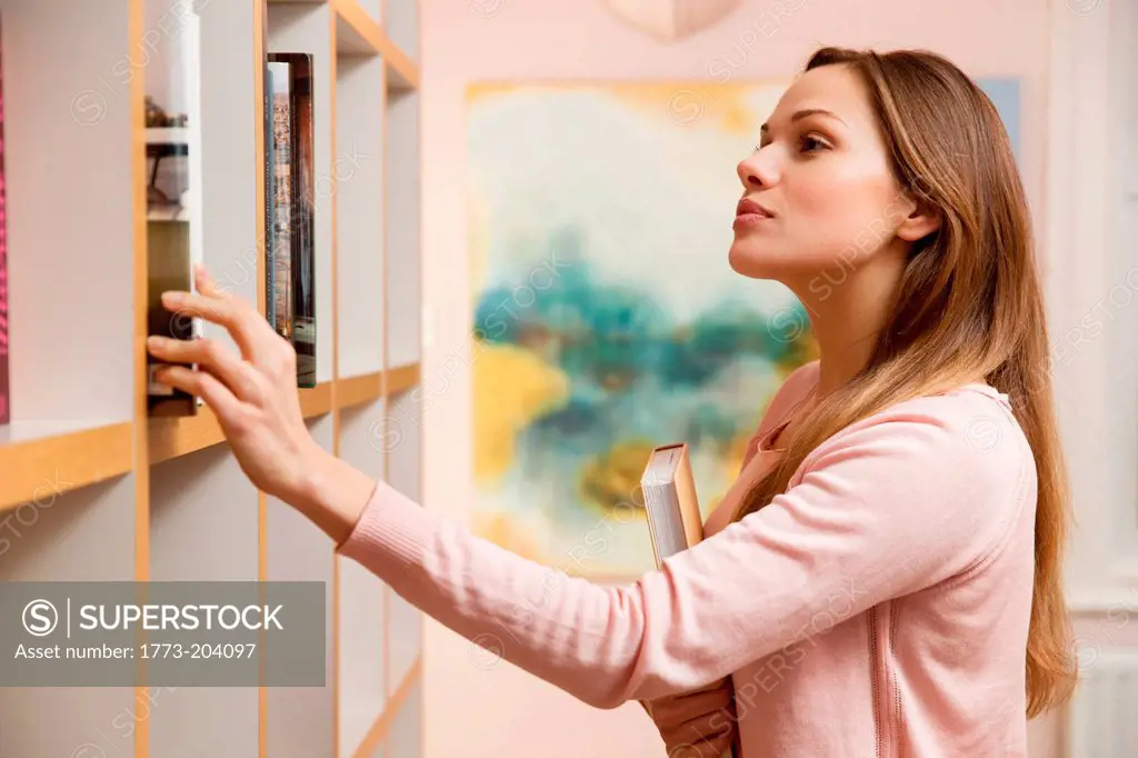 Young woman choosing book from bookcase